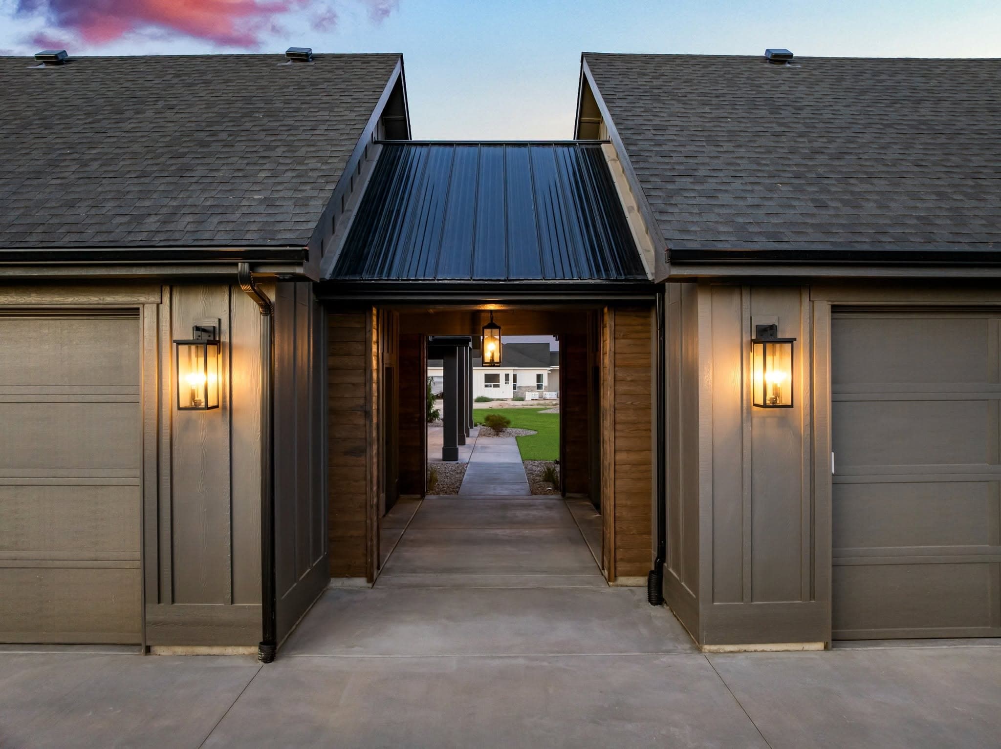 Lantern-lit breezeway between the garage bays of a TKO custom home at dusk, with a lawn and neighboring home beyond