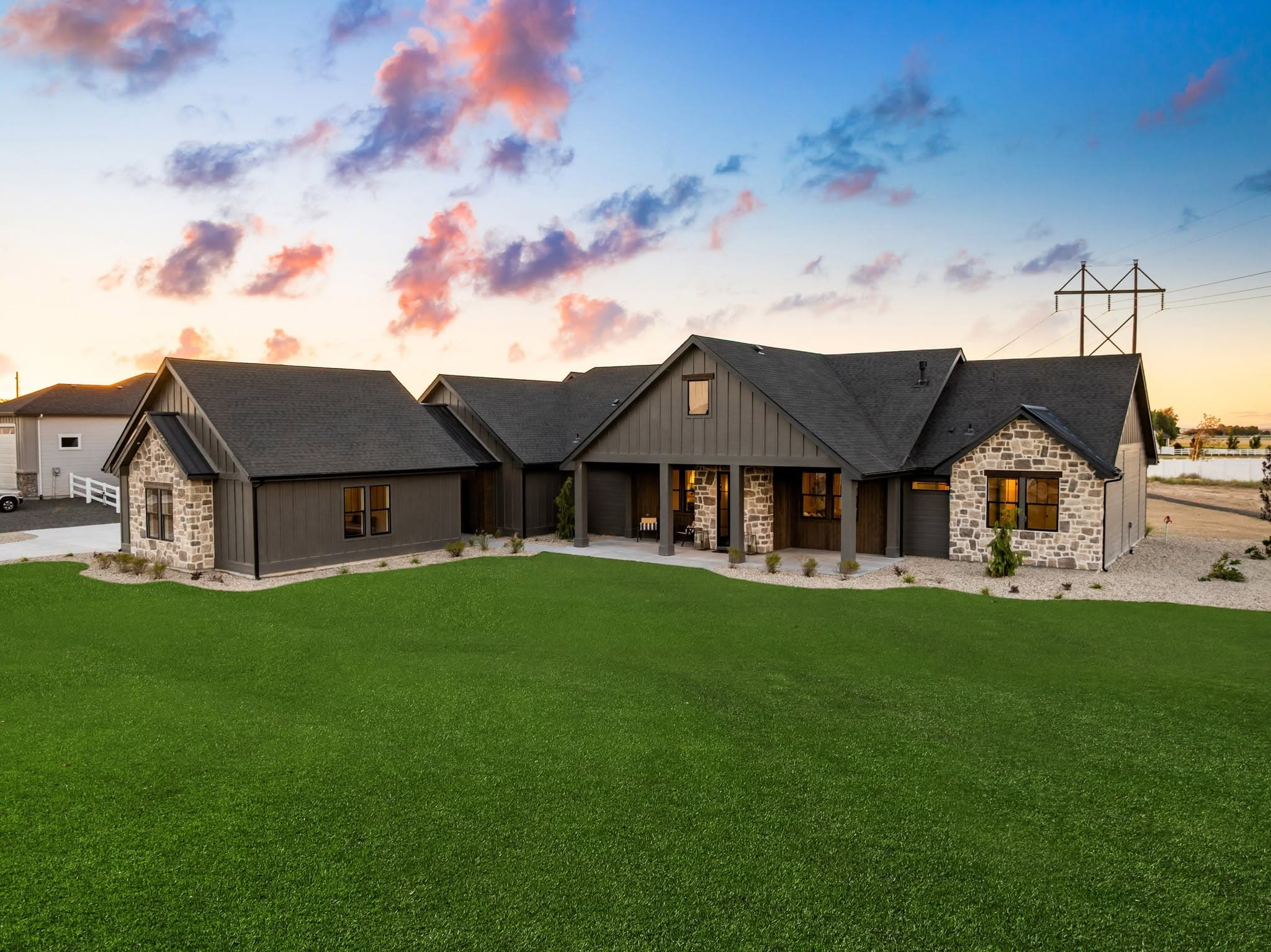 Custom home at dusk with dark board-and-batten siding, stone accents, and a covered patio