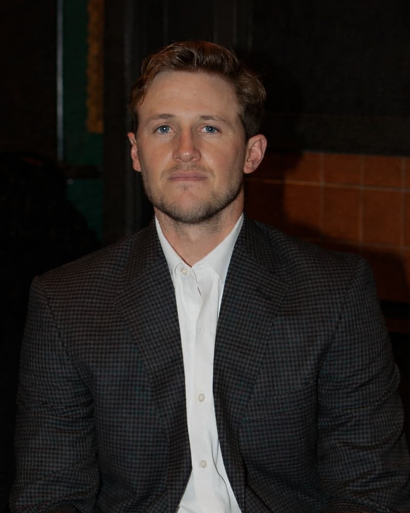 Hunter Ostrom, General Manager of TKO Homes, seated in a dark checked blazer and open-collar white shirt